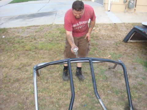 1992 Ford Bronco - A man sprays a metal roll cage with black paint outdoors.