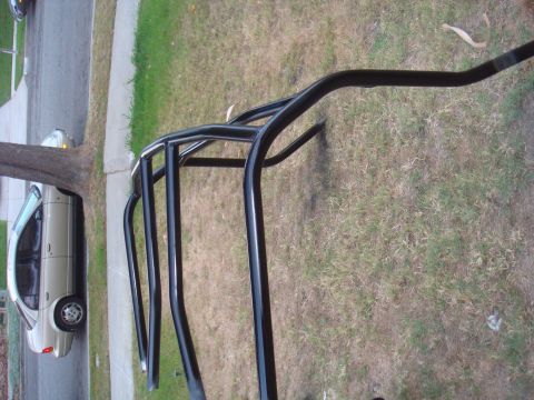 1992 Ford Bronco - A black roll cage is shown in the foreground with a beige sedan parked on a street in the background.