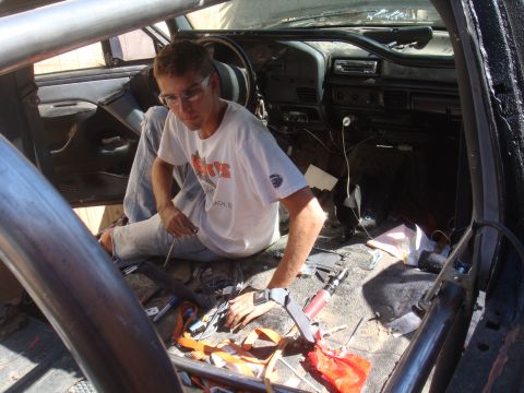 1992 Ford Bronco - A person is working on the interior of a vehicle, surrounded by tools and exposed wiring, with a roll cage visible.