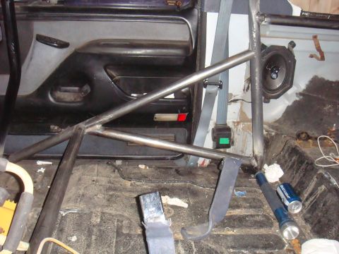 1992 Ford Bronco - The interior of a vehicle is shown, a prominent roll cage, seatbelts, and a speaker mounted on the interior panel.