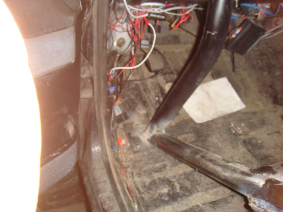 Interior shot of a vehicle showing a roll cage and a mess of wires and electrical components on the floor