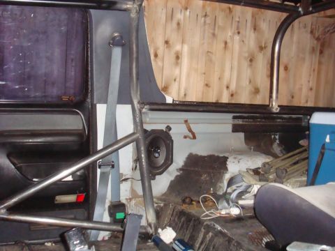 1992 Ford Bronco - The interior of a vehicle shows a roll cage, a speaker mounted on the side panel, and a seatbelt.