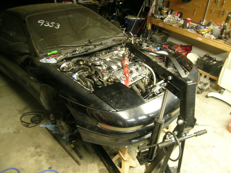 black coupe on jack stands, engine out, being worked on in garage