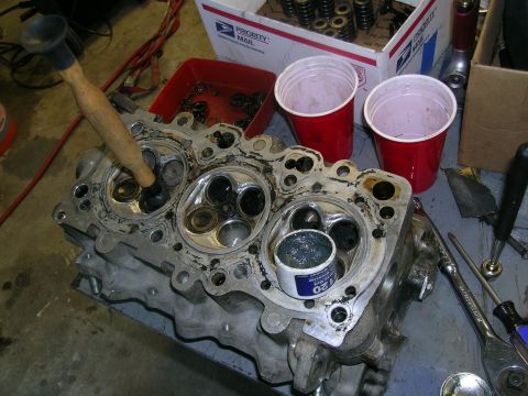 1995 Ford Probe - A disassembled engine cylinder head is shown on a workbench, with tools and parts scattered around.