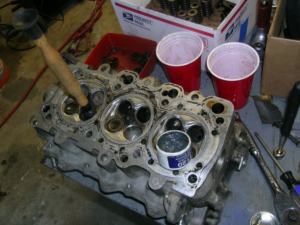 Engine cylinder head with valves and a mallet, on a workbench with tools and cups