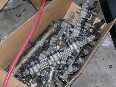 1995 Ford Probe - A cardboard box is filled with numerous fuel injectors and fuel rails, some with black plastic components.