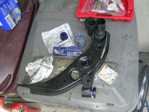 1995 Ford Probe - A control arm and associated suspension components, including bushings and a ball joint, are laid out on a surface.