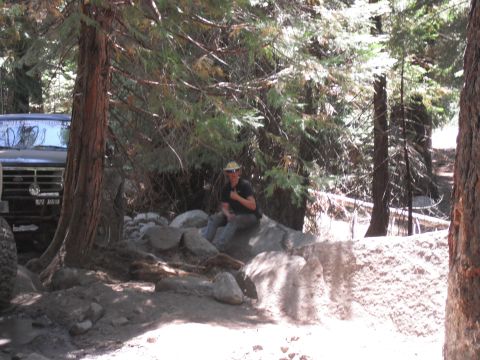 1991 Ford Bronco - A 1991 Ford Bronco is parked off-road in a wooded area with a person sitting on rocks nearby.