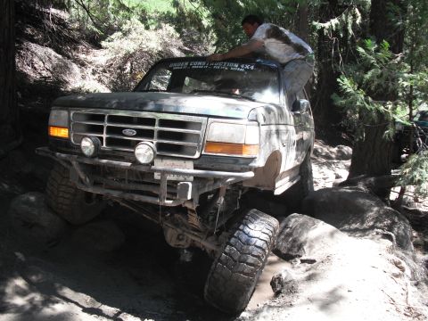 1991 Ford Bronco - Ford Bronco tackling a challenging rocky trail with a person assisting from the roof.