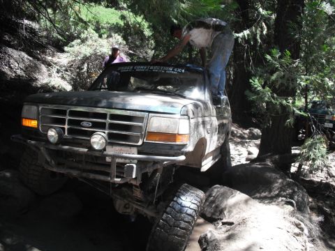 1991 Ford Bronco - A Ford truck navigates a difficult off-road path with a person on its roof.