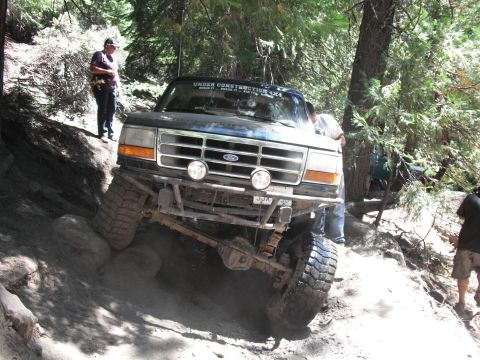 1991 Ford Bronco - A modified Ford truck is shown tackling a steep, rocky off-road path with people observing.