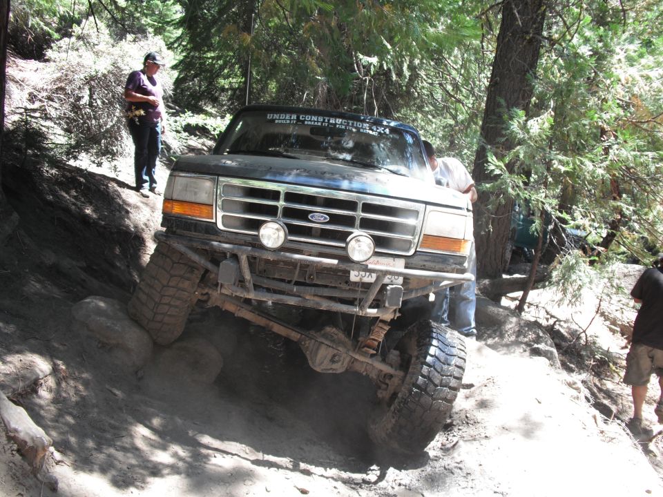 Ford truck navigating rocky trail, front view. Windshield banner says 'UNDER CONSTRUCTION 4X4'