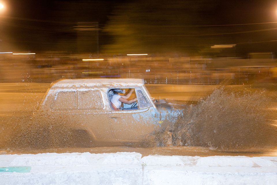 SUV driving through mud, splashing water everywhere. Driver visible inside
