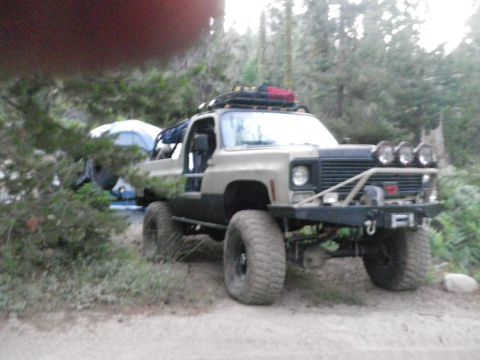 1991 Ford Bronco - This modified SUV is set up for camping in a forest with a tent visible behind it.