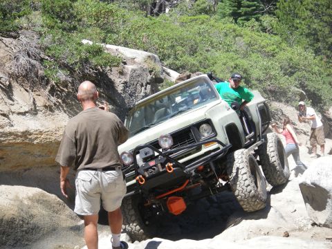1991 Ford Bronco - This heavily modified SUV is tackling a challenging rocky trail with onlookers observing the action.