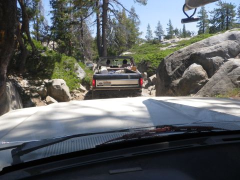 1991 Ford Bronco - Two vehicles navigate a , wooded off-road path with large boulders.