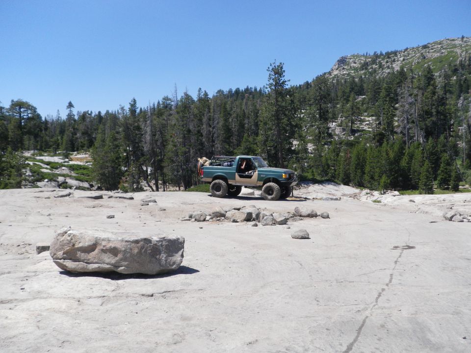 Green and tan Ford Bronco with off-road tires parked on a rocky, barren landscape