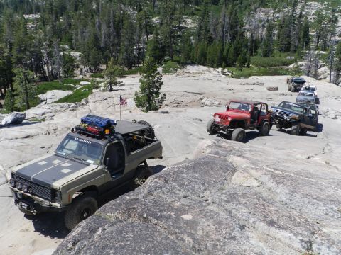 1991 Ford Bronco - A convoy of off-road vehicles traverses a challenging rocky trail in a mountainous area.