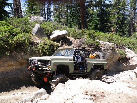 1991 Ford Bronco - Modified pickup truck navigates a rocky trail with a spare tire mounted at the rear.