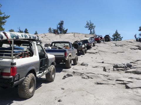 1991 Ford Bronco - Several off-road vehicles are navigating a steep, rocky incline under a clear blue sky.