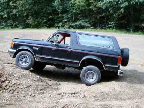 1989 Ford Bronco - This black Ford Bronco is parked on a dirt path, with a spare tire mounted on the rear.