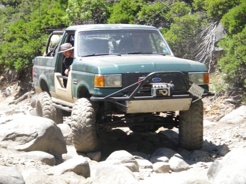 1991 Ford Bronco - This modified Ford truck is tackling a rocky trail with its driver visible.