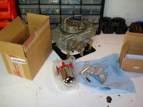 1984 Ford Bronco - A new four-barrel carburetor sits on a black spacer plate on a white workbench, with gold-anodized studs and a Summit Racing shipping box o…