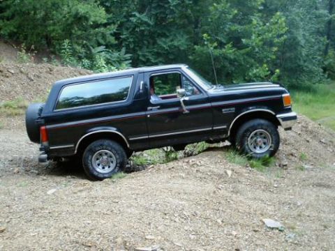 1989 Ford Bronco - A black Ford Bronco navigates a dirt path in a wooded area.