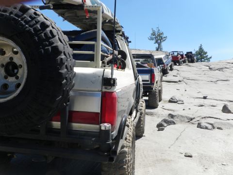 1991 Ford Bronco - Several off-road vehicles, including a 1991 Ford Bronco, are lined up on a rocky path under a clear blue sky.