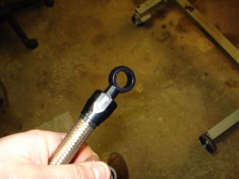 1984 Ford Bronco - A hand holds up the end of a braided stainless steel hose fitted with a black anodized AN hose end and a banjo-style ring fitting. The conc…