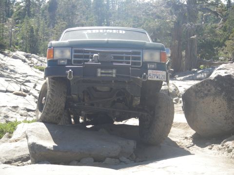 1991 Ford Bronco - This modified Ford truck is navigating a rocky trail with its front tires on large boulders.