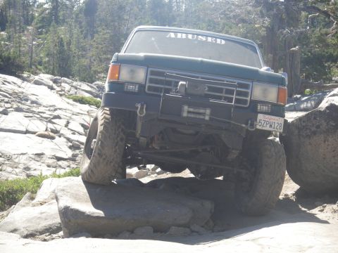 1991 Ford Bronco - This modified off-road vehicle navigates a challenging rocky path, displaying a custom "ABUSED" decal on its windshield.
