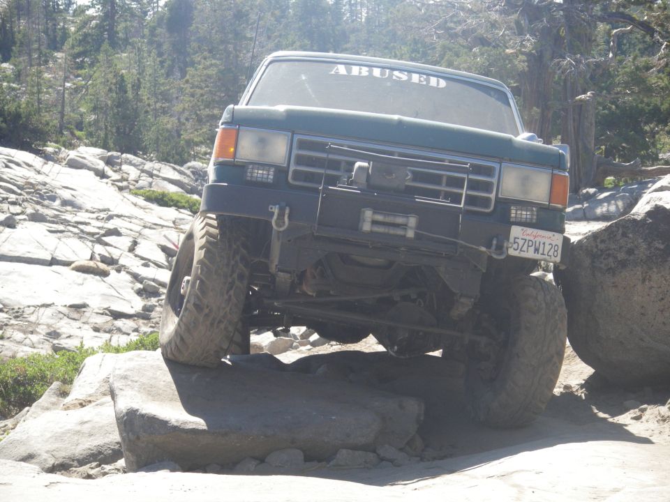 Green off-road vehicle with "ABUSED" sticker on windshield, navigating rocky terrain