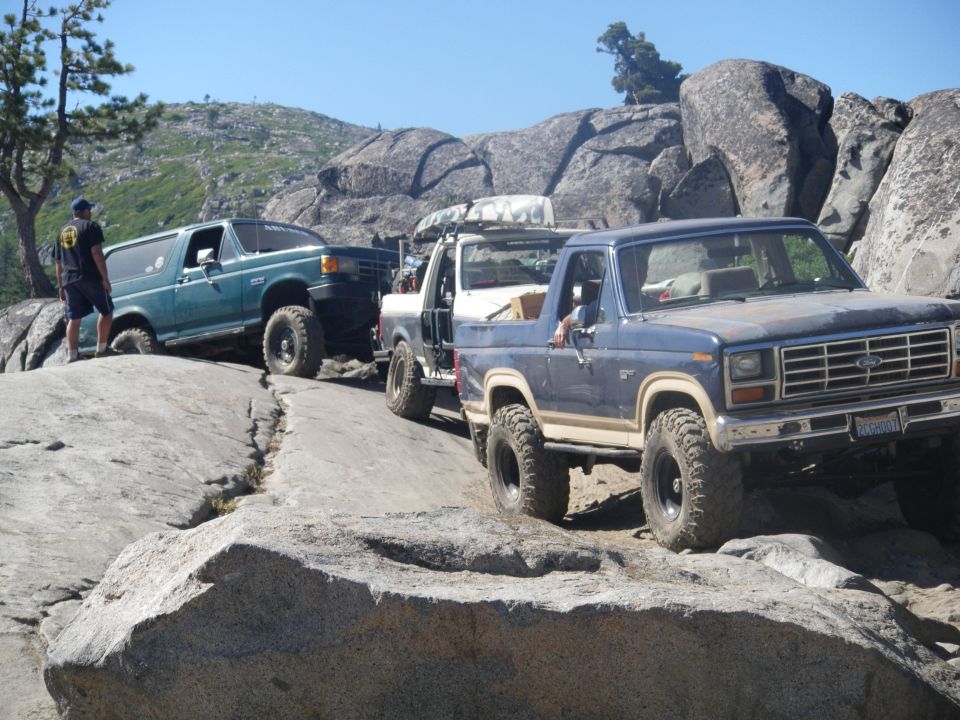 Blue 1980s Ford Bronco, green Ford Bronco, and white pickup truck on a rocky off-road trail