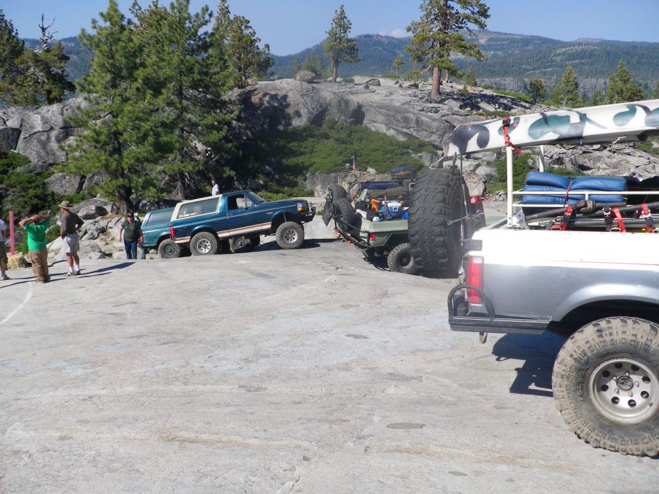 Blue 1991 Ford Bronco parked on rocky terrain with a trailer and another truck behind it