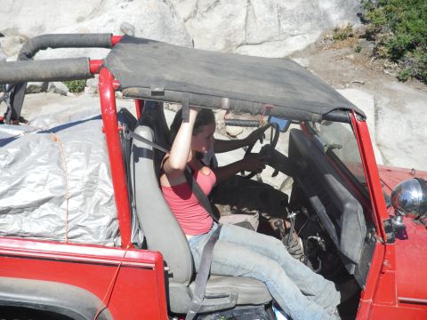 1991 Ford Bronco - A woman drives a red off-road vehicle, with seatbelts secured, on a rocky terrain.