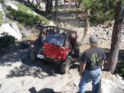 1991 Ford Bronco - A red Jeep Wrangler navigates a challenging rocky trail with a person watching.