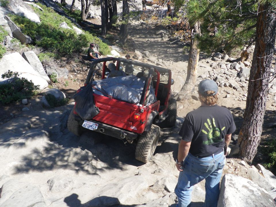 Red Jeep Wrangler on rocky trail, rear view, license plate 6BQP541