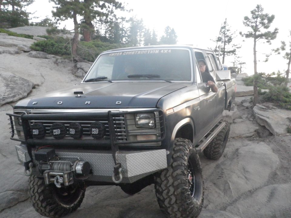 Dark gray Ford F-Series truck with custom bumper and KC lights off-roading