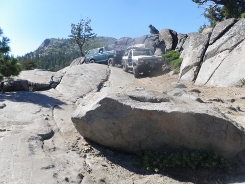1991 Ford Bronco - Two off-road vehicles navigate a challenging rocky trail under a clear blue sky.