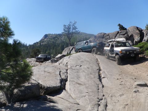 1991 Ford Bronco - Multiple off-road vehicles navigate a steep, rocky trail under a clear blue sky.