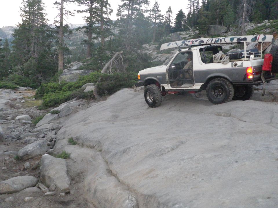 White and grey 1991 Ford Bronco with doors open, canoe on roof, driving on rocky terrain