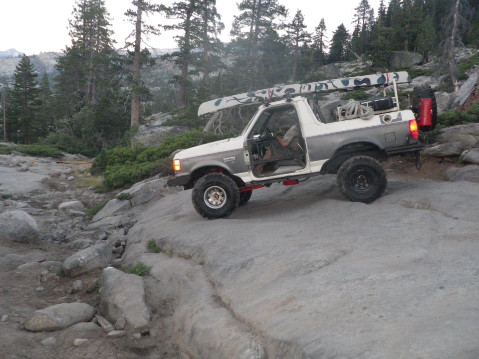 White and grey 1991 Ford Bronco off-roading with a canoe on the roof