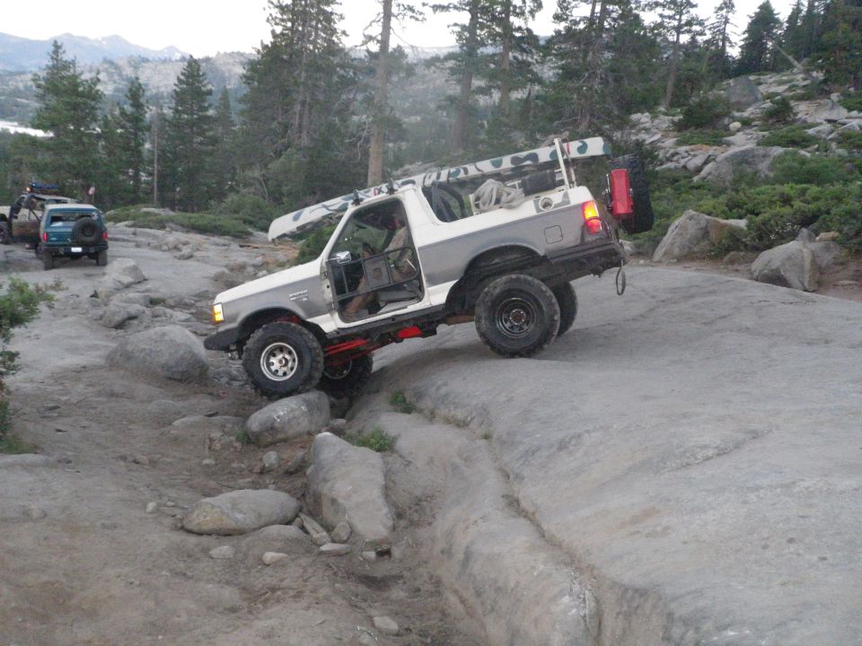 White and gray 1991 Ford Bronco with doors removed, navigating a rocky trail with a canoe on the roof rack