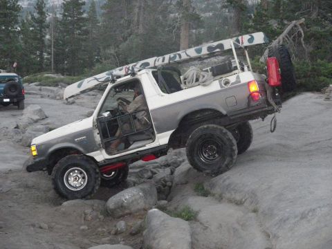 1991 Ford Bronco - A 1991 Ford Bronco navigates a rocky trail with a canoe secured to its roof rack.