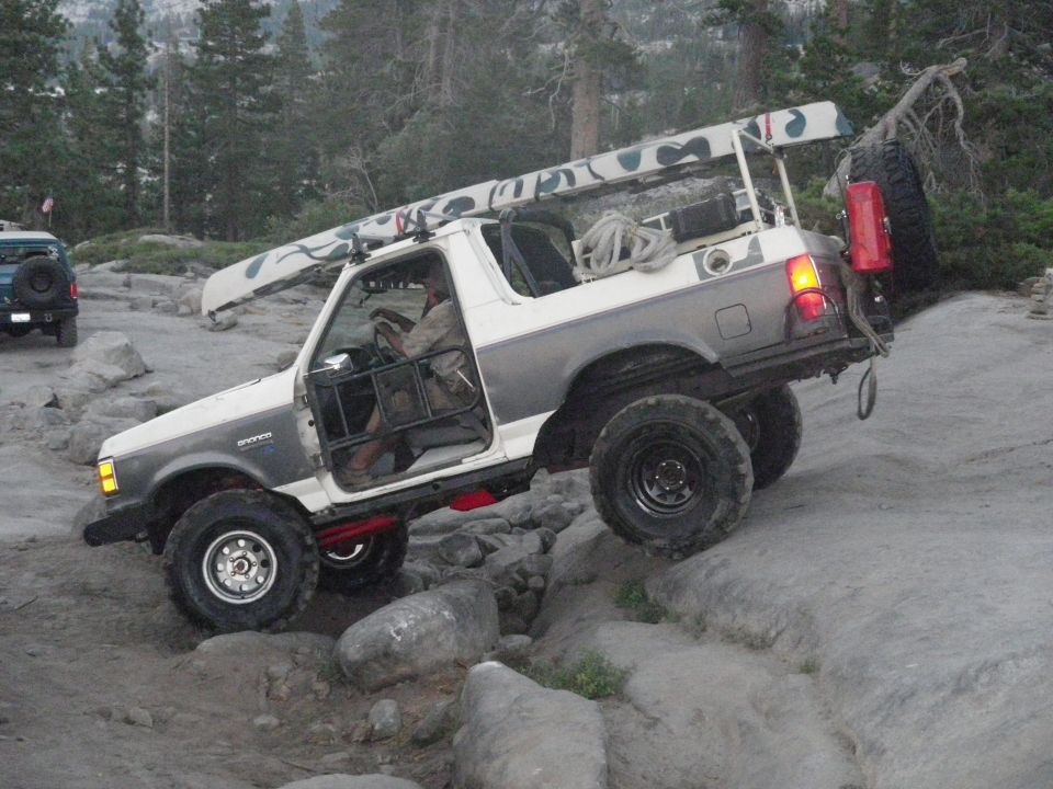 1991 Ford Bronco navigating rocky terrain, canoe on roof rack, spare tire mounted on rear door