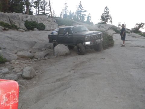 1991 Ford Bronco - A black pickup truck navigates a rocky, off-road path with a person standing nearby.