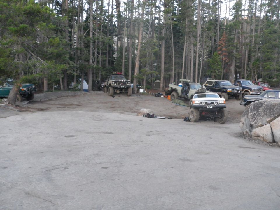 White 1991 Ford Bronco front view, parked with other off-road vehicles in a forest
