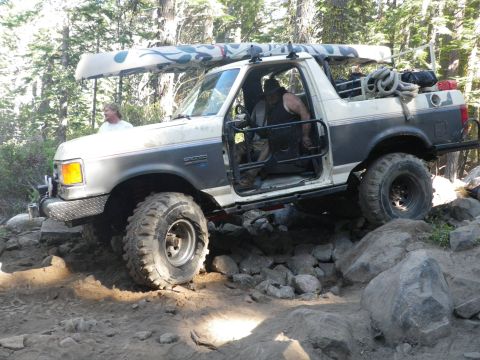 1991 Ford Bronco - A modified Ford Bronco is shown traversing a difficult, rocky trail with a canoe secured to its roof rack.
