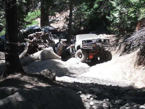 1991 Ford Bronco - Off-road vehicles traverse a challenging rocky and sandy trail in a wooded area.